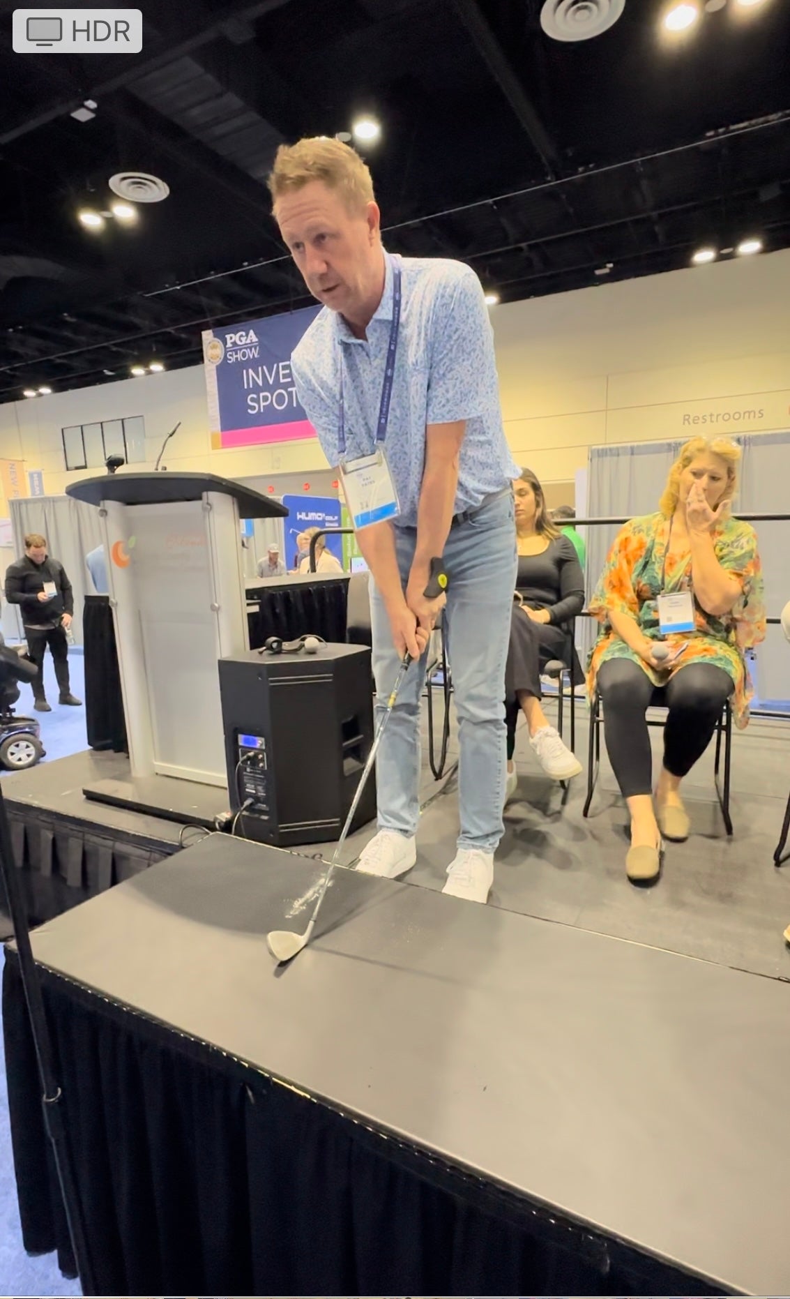 Golfer demonstrating with a club and ZoneGrip at the 2024 PGA Show Inventors Spotlight, PGA Show sign behind